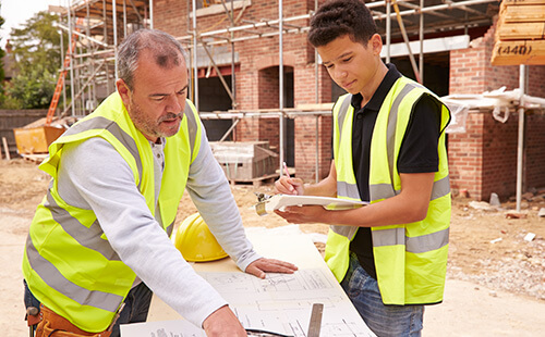 Builder on building site discussing work with apprentice